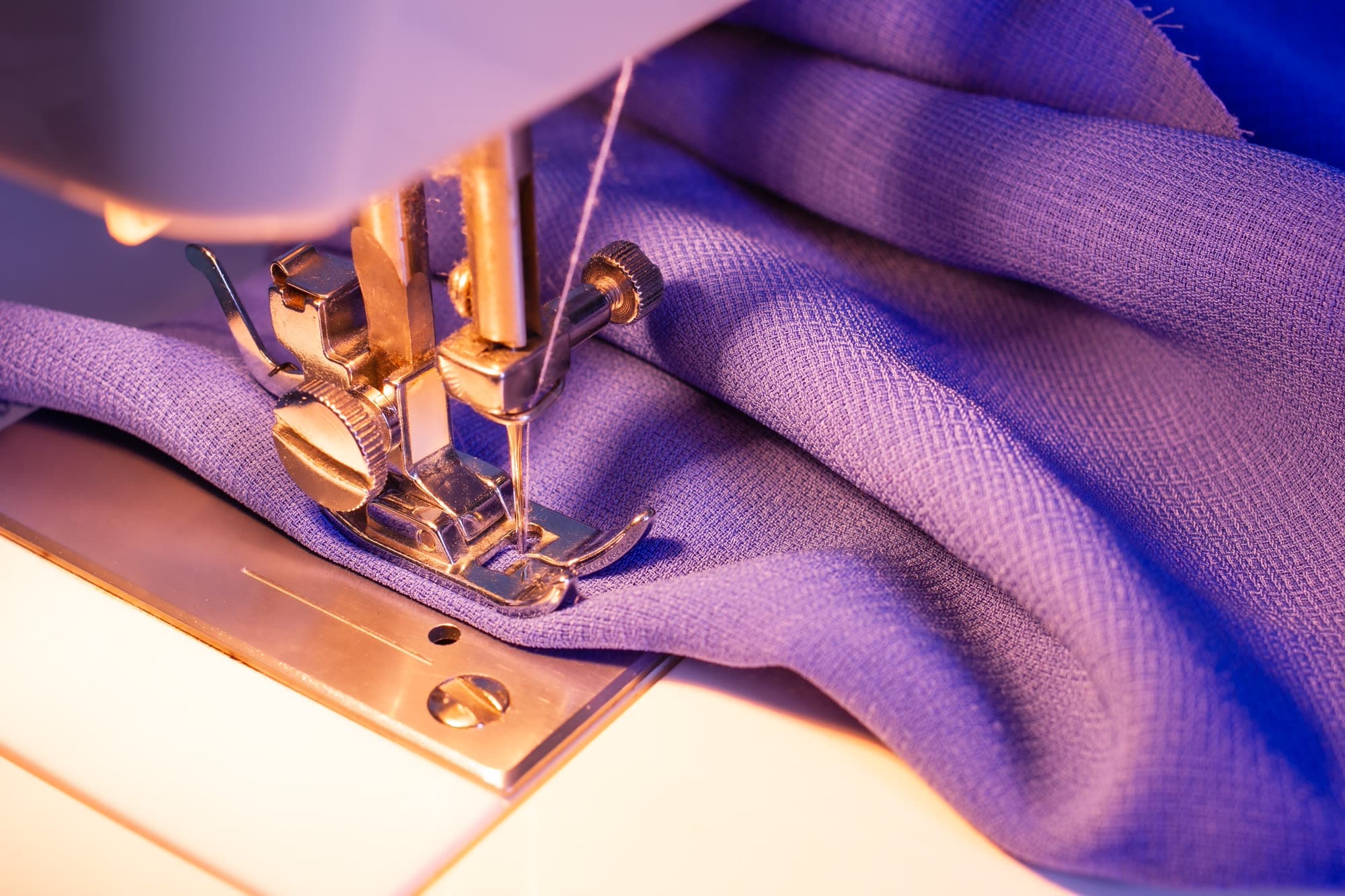 Primer plano del prensatelas de una máquina de coser cosiendo una tela malva.